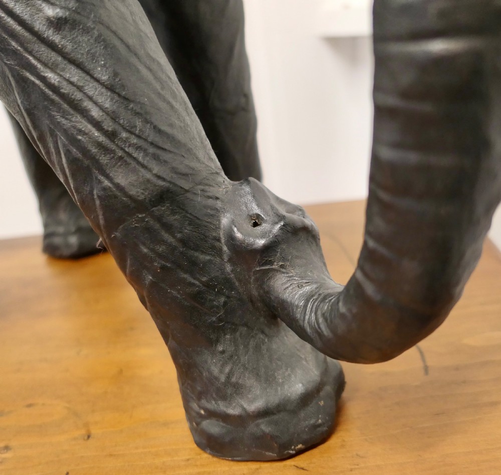 A dark brown moulded leather model of a standing bull elephant with realistic skin texture and light-coloured tusks. View III