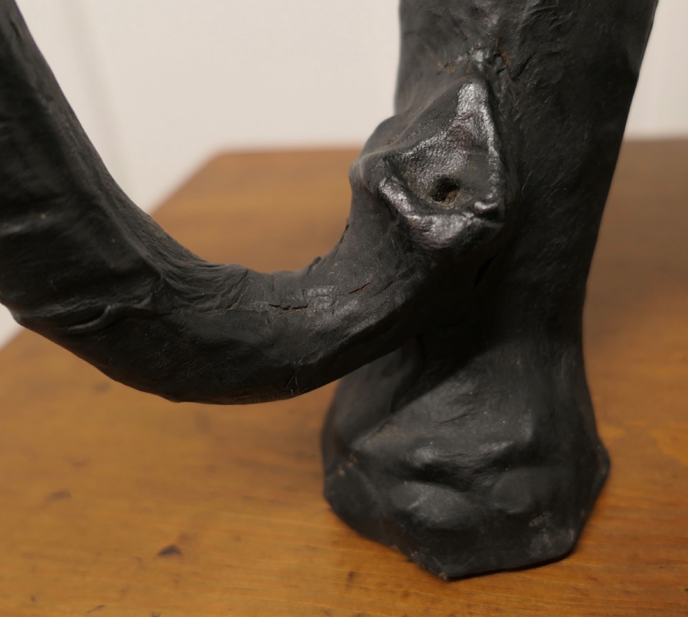 A dark brown moulded leather model of a standing bull elephant with realistic skin texture and light-coloured tusks. View IV