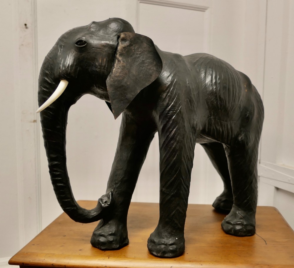 A dark brown moulded leather model of a standing bull elephant with realistic skin texture and light-coloured tusks. View V