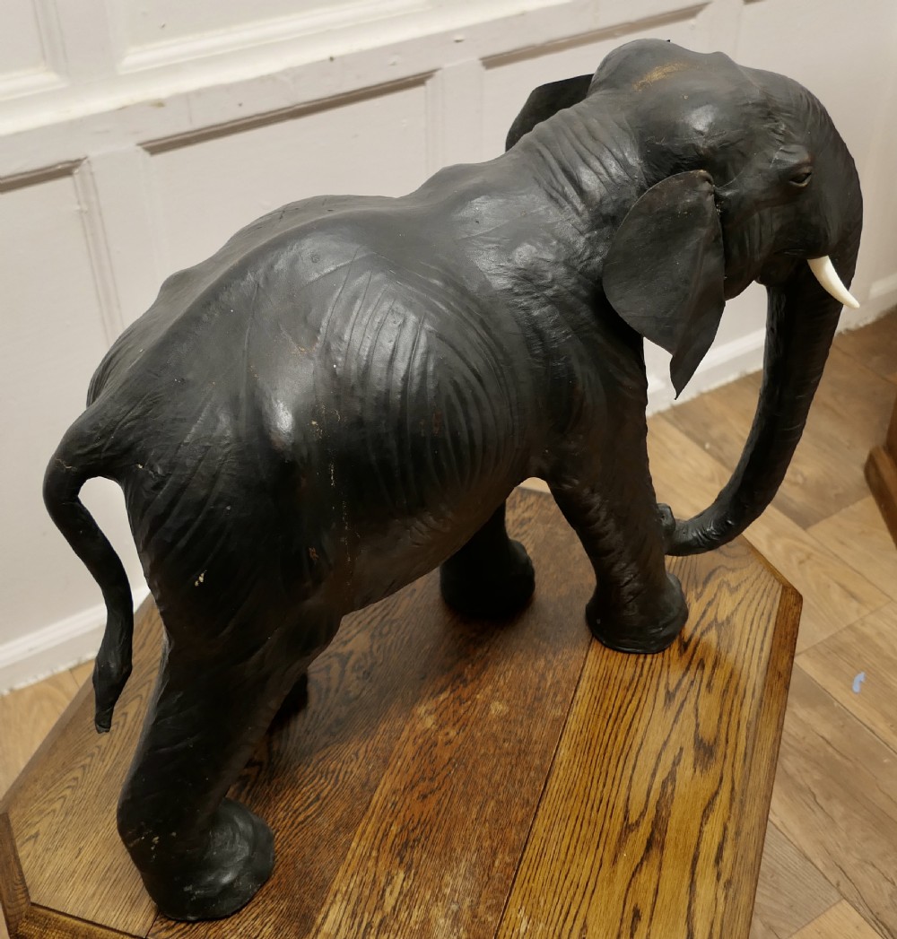 A dark brown moulded leather model of a standing bull elephant with realistic skin texture and light-coloured tusks. View VII