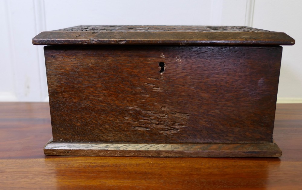 A dark carved oak correspondence box featuring a hinged lid with carved relief detail, a front keyhole, and a moulded rectangular base.