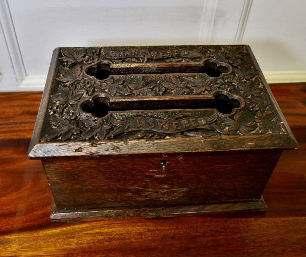 A dark carved oak correspondence box featuring a hinged lid with carved relief detail, a front keyhole, and a moulded rectangular base. View II