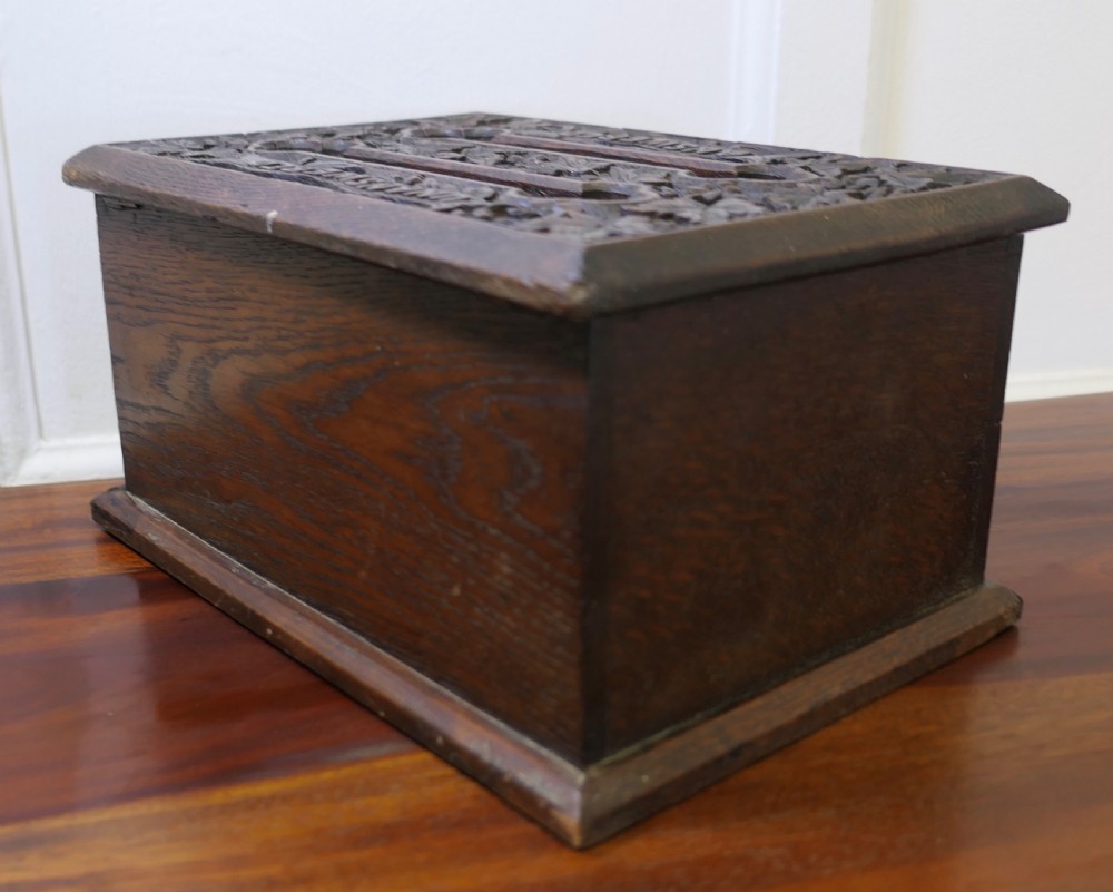 A dark carved oak correspondence box featuring a hinged lid with carved relief detail, a front keyhole, and a moulded rectangular base. View V