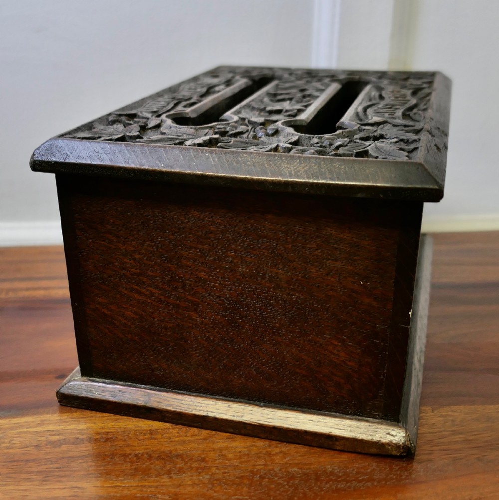 A dark carved oak correspondence box featuring a hinged lid with carved relief detail, a front keyhole, and a moulded rectangular base. View VI
