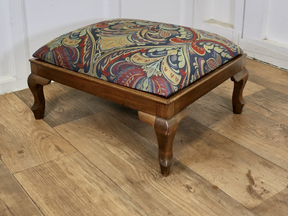 A low rectangular Victorian footstool featuring carved wooden cabriole legs and a padded cushion upholstered in a colourful paisley pattern.