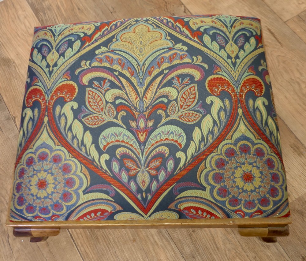 A low rectangular Victorian footstool featuring carved wooden cabriole legs and a padded cushion upholstered in a colourful paisley pattern. View V
