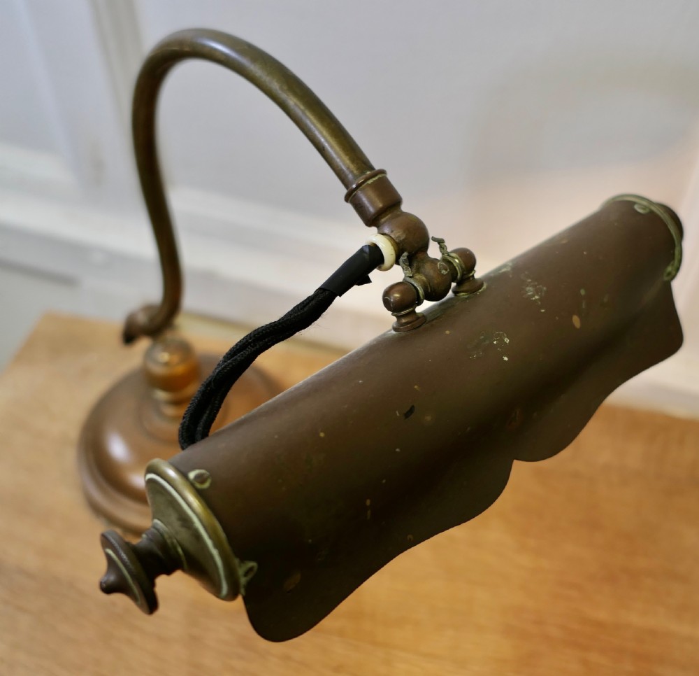 An antique brass desk lamp featuring a curved gooseneck stem, a circular weighted base, and an adjustable scalloped shade. View VII