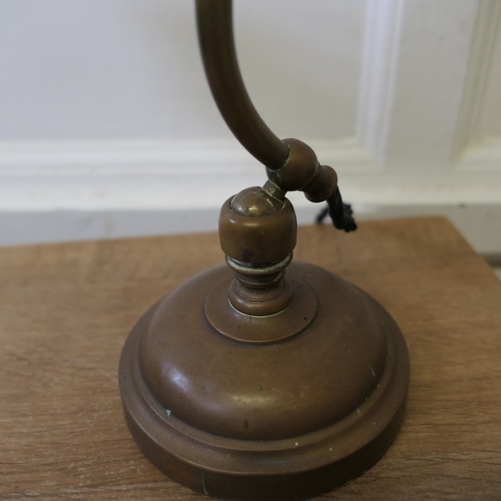 An antique brass desk lamp featuring a curved gooseneck stem, a circular weighted base, and an adjustable scalloped shade. View XII