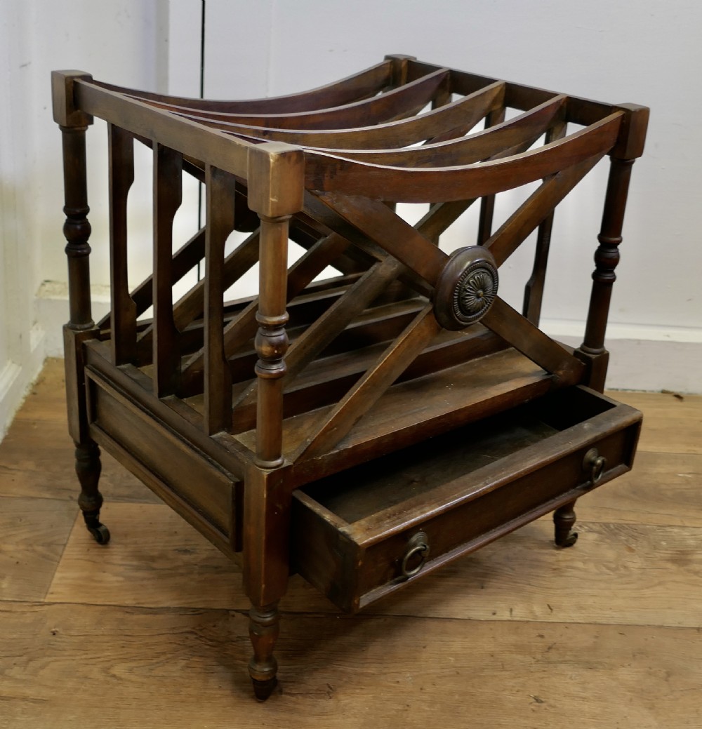 A mahogany Regency style Canterbury featuring X-frame dividers with carved central rosettes, turned posts, a single drawer, and brass castors. View VII