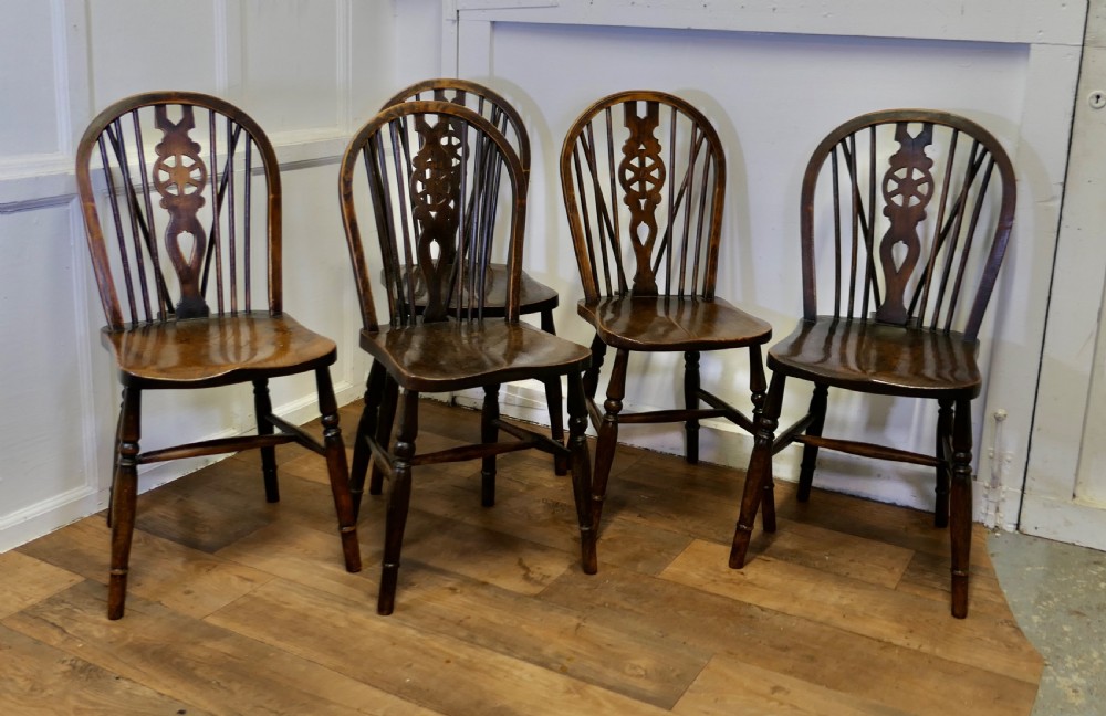 A set of five dark brown Victorian Windsor dining chairs with pierced wheelback central splats, hoop backs, and turned legs.