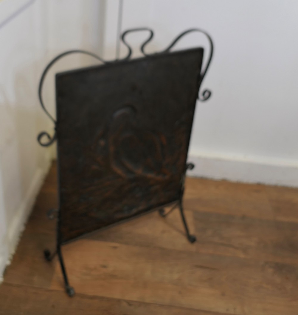 An Arts and Crafts wrought iron fire screen with a hammered copper panel depicting a repousse stork catching a fish near water. View VI
