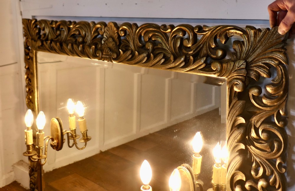 A large rectangular gold giltwood framed mirror featuring elaborate carved scrolling foliage and twin integrated candle sconces. View VII