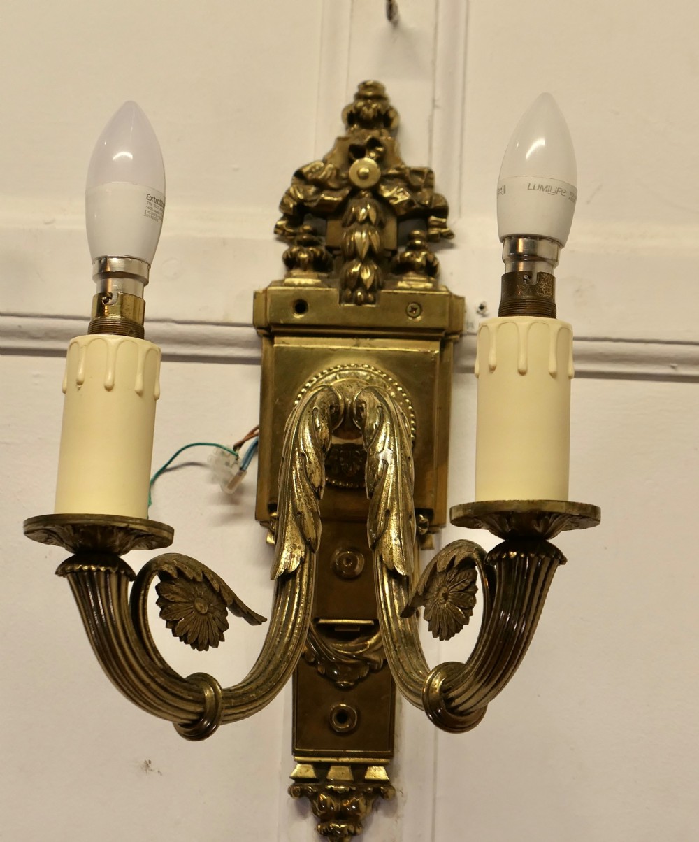 A pair of Neoclassical cast brass twin-arm wall lights with decorative backplates, acanthus leaf details, and candle sleeves. View II