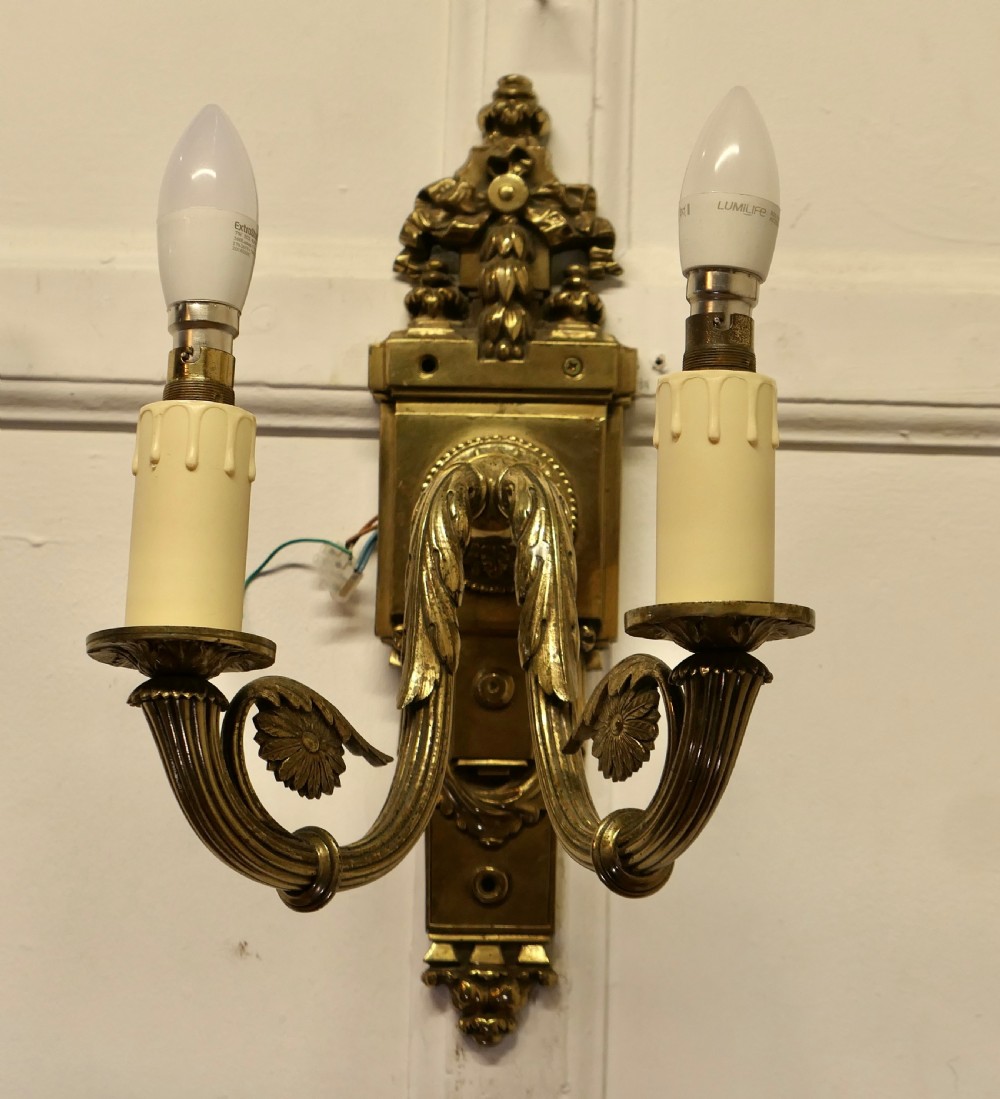 A pair of Neoclassical cast brass twin-arm wall lights with decorative backplates, acanthus leaf details, and candle sleeves. View III