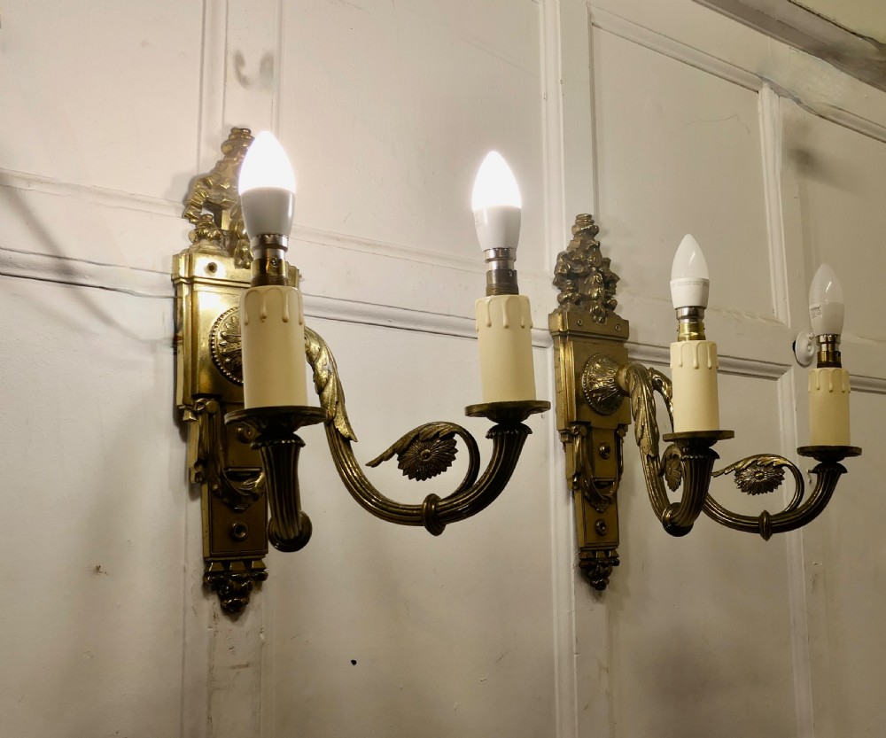 A pair of Neoclassical cast brass twin-arm wall lights with decorative backplates, acanthus leaf details, and candle sleeves. View VIII