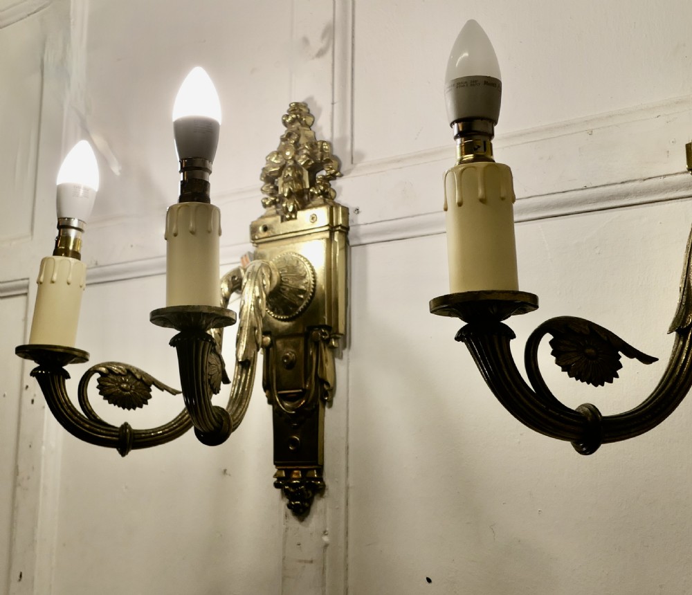 A pair of Neoclassical cast brass twin-arm wall lights with decorative backplates, acanthus leaf details, and candle sleeves. View XI