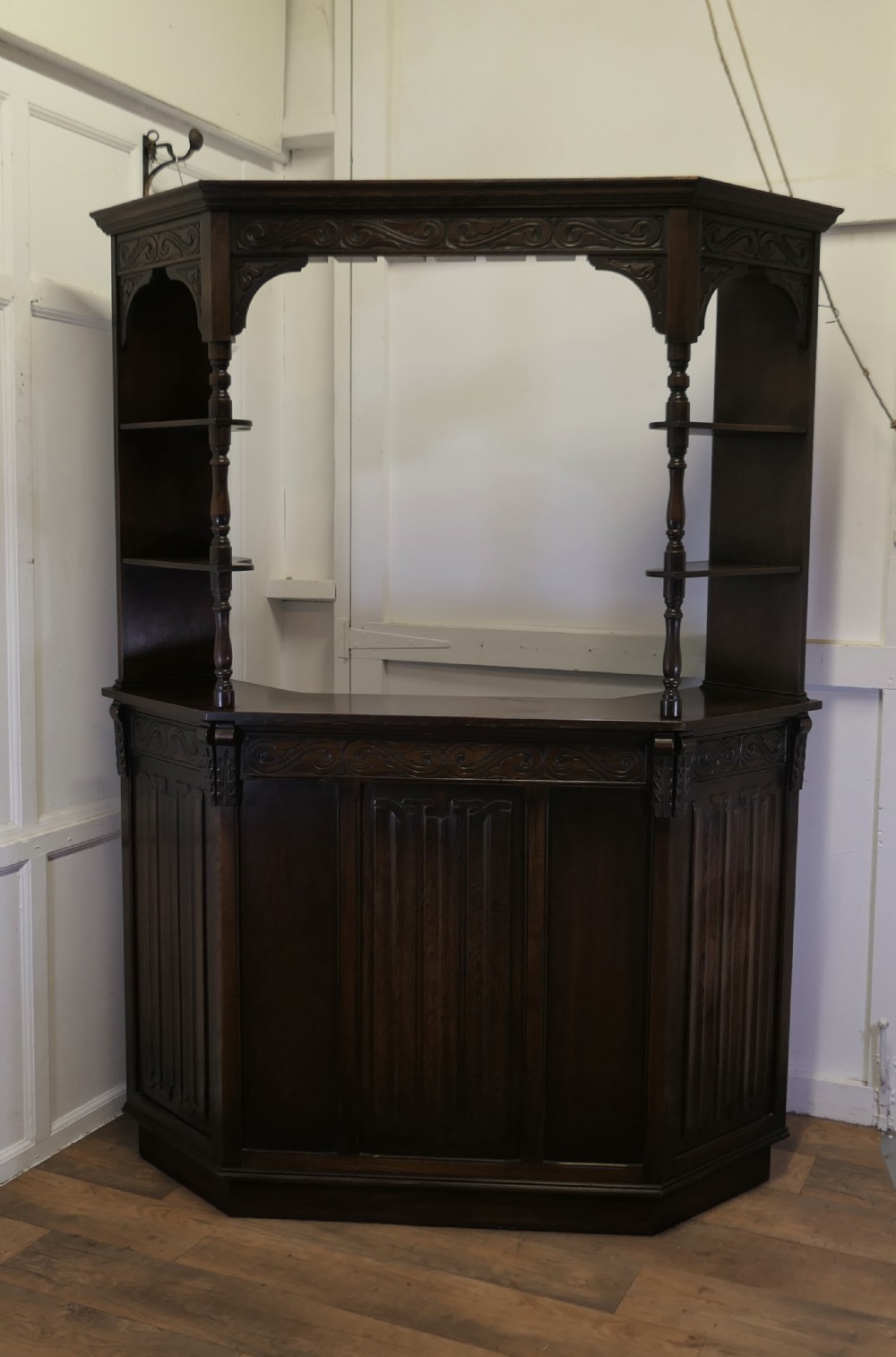 A dark brown carved oak canopy bar featuring turned spindle columns, open side shelves, an overhead frieze, and vertical panelled detailing on the base.