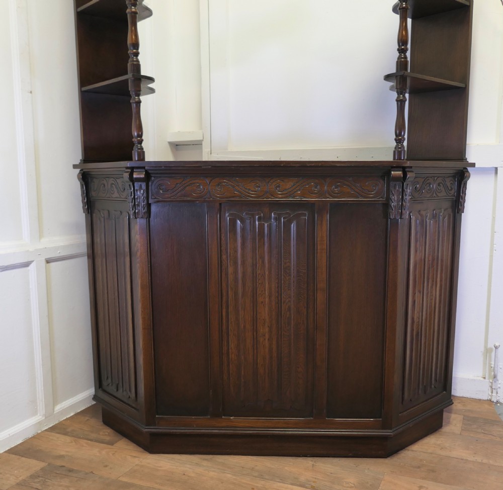 A dark brown carved oak canopy bar featuring turned spindle columns, open side shelves, an overhead frieze, and vertical panelled detailing on the base. View II