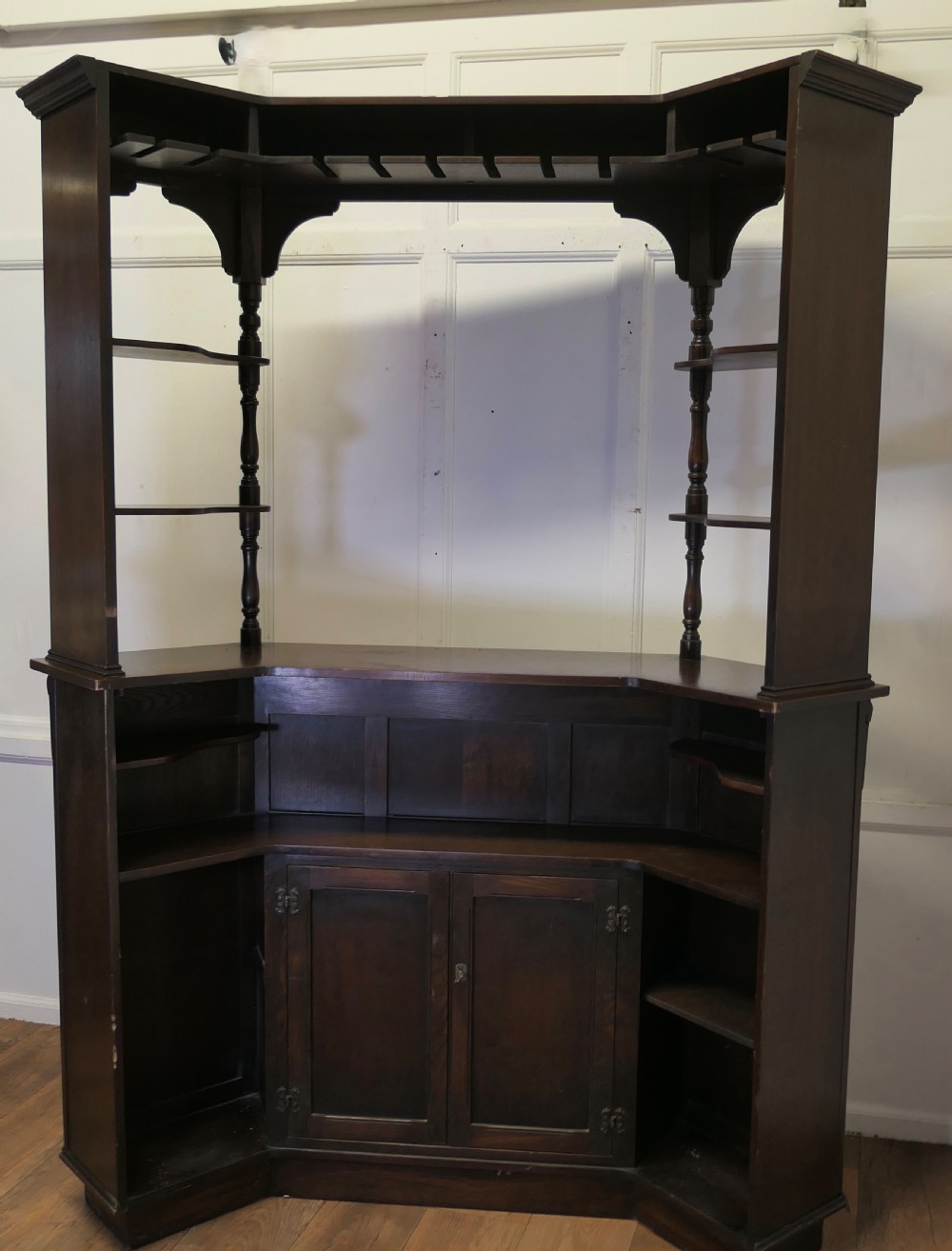A dark brown carved oak canopy bar featuring turned spindle columns, open side shelves, an overhead frieze, and vertical panelled detailing on the base. View VI