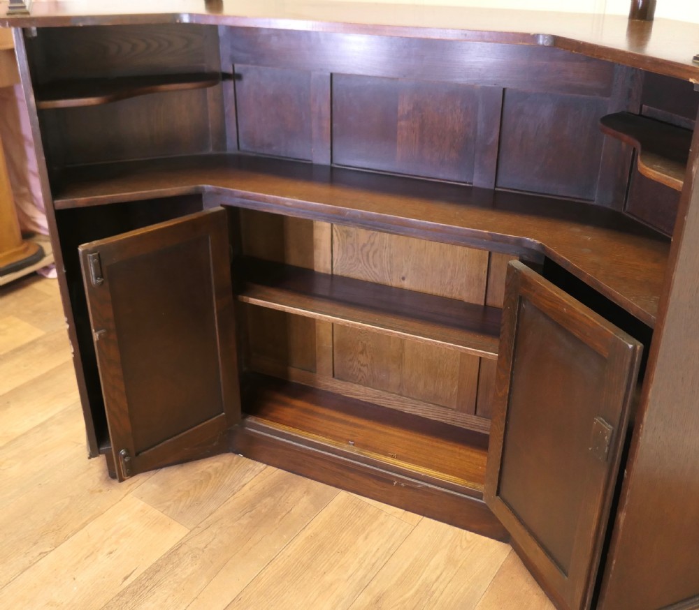 A dark brown carved oak canopy bar featuring turned spindle columns, open side shelves, an overhead frieze, and vertical panelled detailing on the base. View X