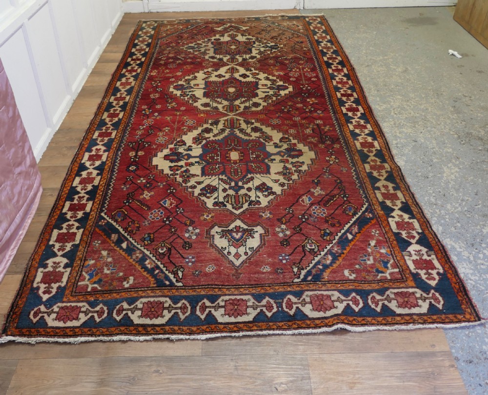 A large red wool carpet featuring traditional central medallion designs, geometric floral motifs, and a navy blue decorative border.