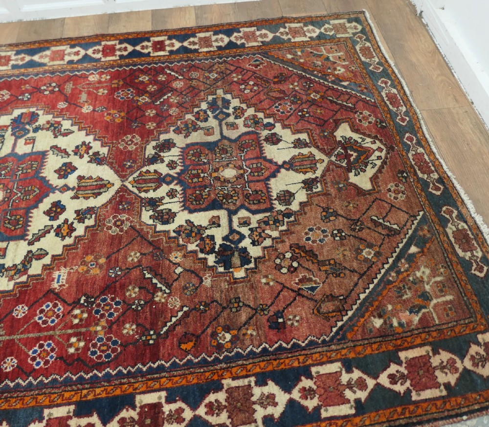 A large red wool carpet featuring traditional central medallion designs, geometric floral motifs, and a navy blue decorative border. View VII