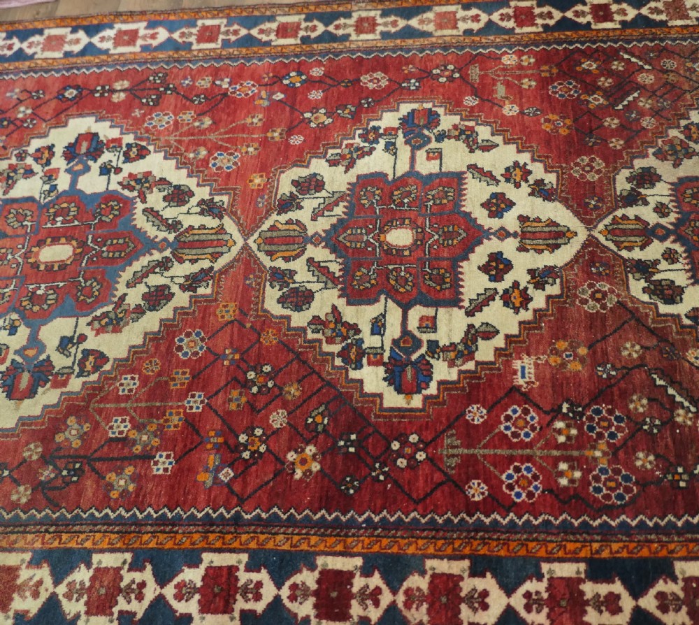 A large red wool carpet featuring traditional central medallion designs, geometric floral motifs, and a navy blue decorative border. View VIII