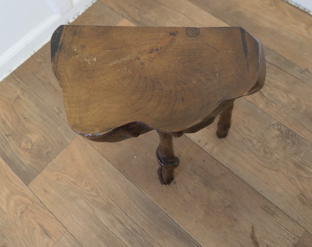 A three-legged dark brown elm stool featuring a thick, live-edge wood slice top supported by natural branch legs. View III