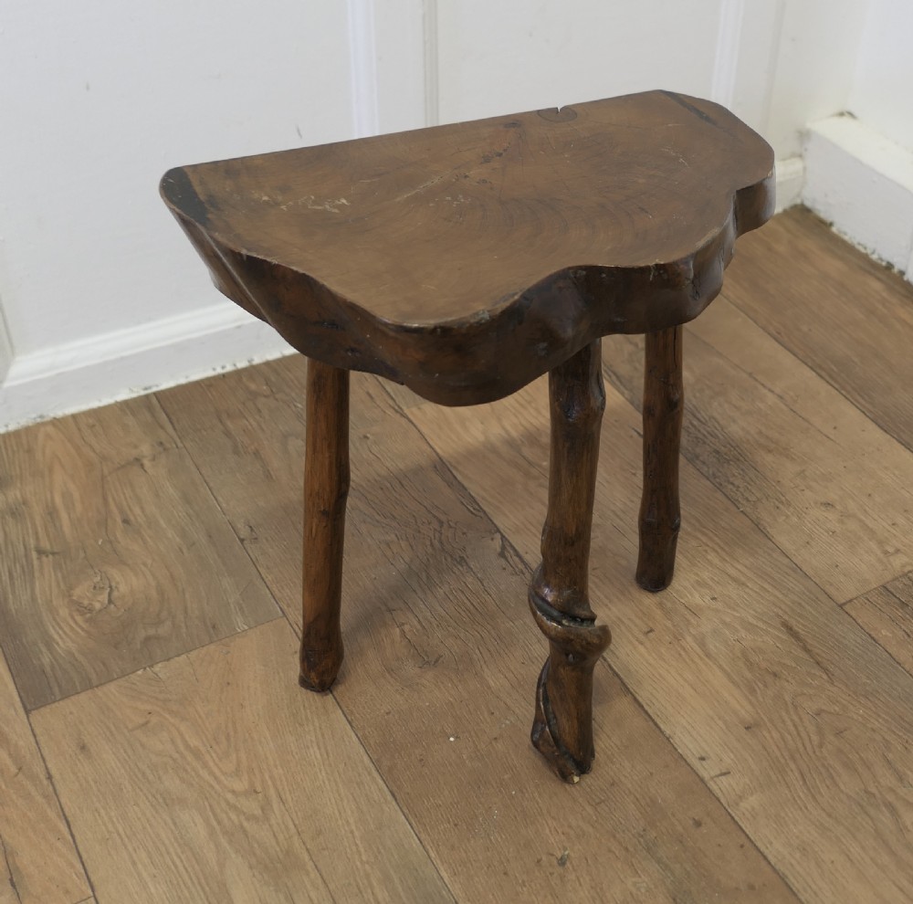 A three-legged dark brown elm stool featuring a thick, live-edge wood slice top supported by natural branch legs. View VI