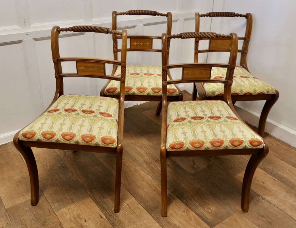 A set of four Art Nouveau walnut dining chairs featuring twisted top rails, inlaid back splats, and floral patterned fabric seats.