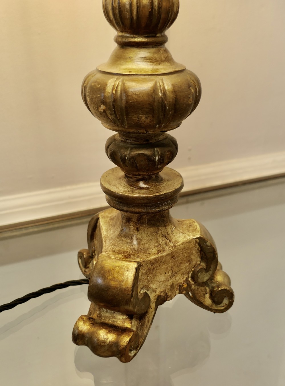 A carved wooden table lamp with a distressed gold finish, standing on scroll feet and topped with a cream fabric lampshade with fringed trim. View III