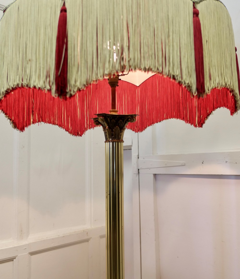 A fluted brass standard floor lamp featuring a tiered red and cream fabric shade with long fringe detail and tassel trim. View IV