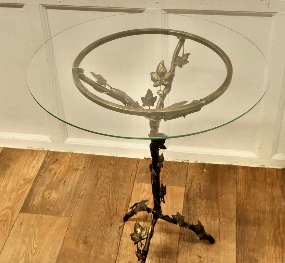 A small circular glass-topped wine table resting on a dark bronze metal tripod base sculpted into trailing ivy vine leaves. View III