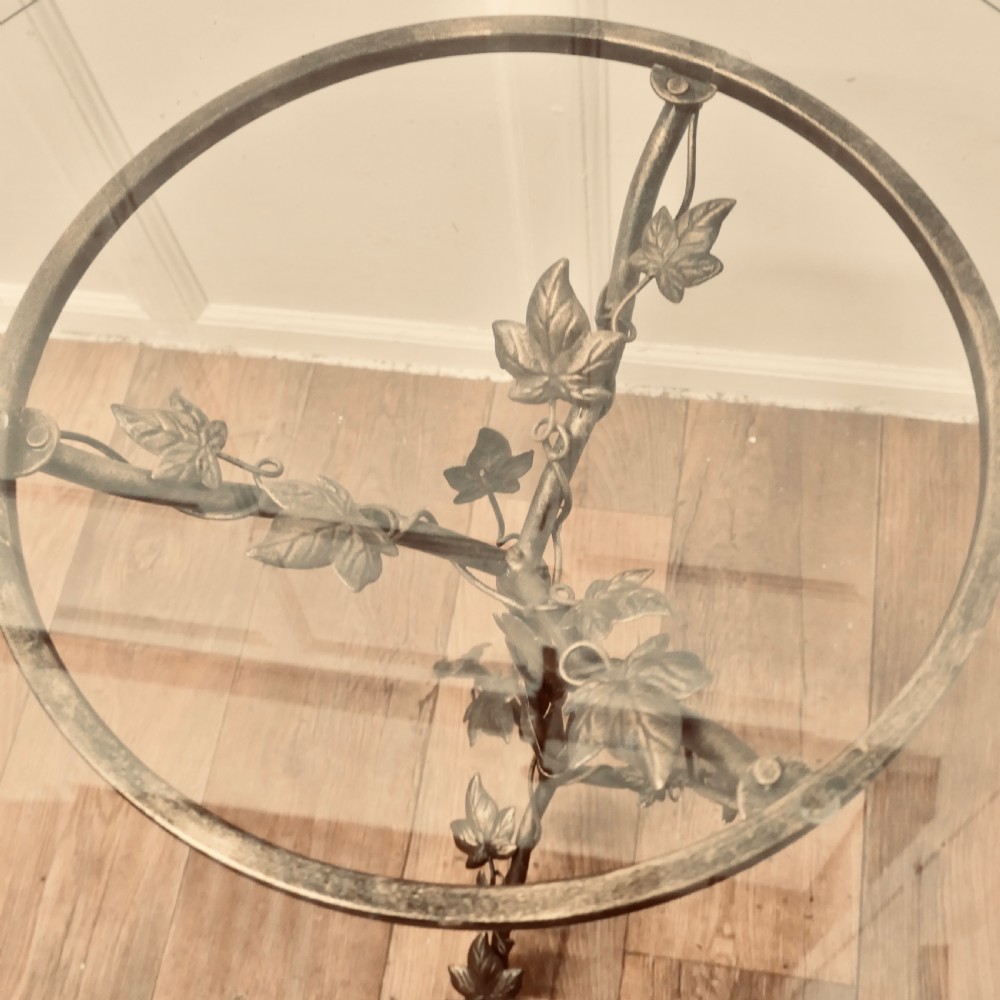 A small circular glass-topped wine table resting on a dark bronze metal tripod base sculpted into trailing ivy vine leaves. View IV