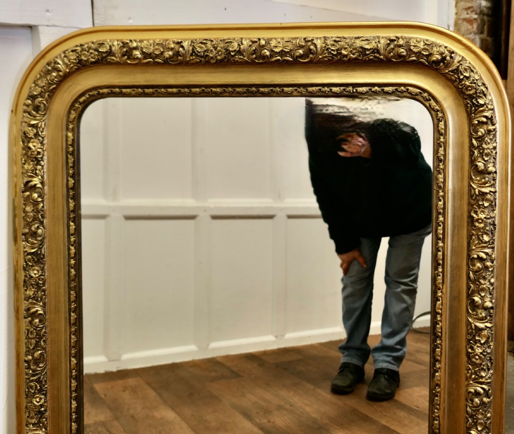 Large 19th-century French Louis Philippe mirror featuring a rounded-top gold leaf frame with detailed floral relief moulding and beaded inner trim. View VI