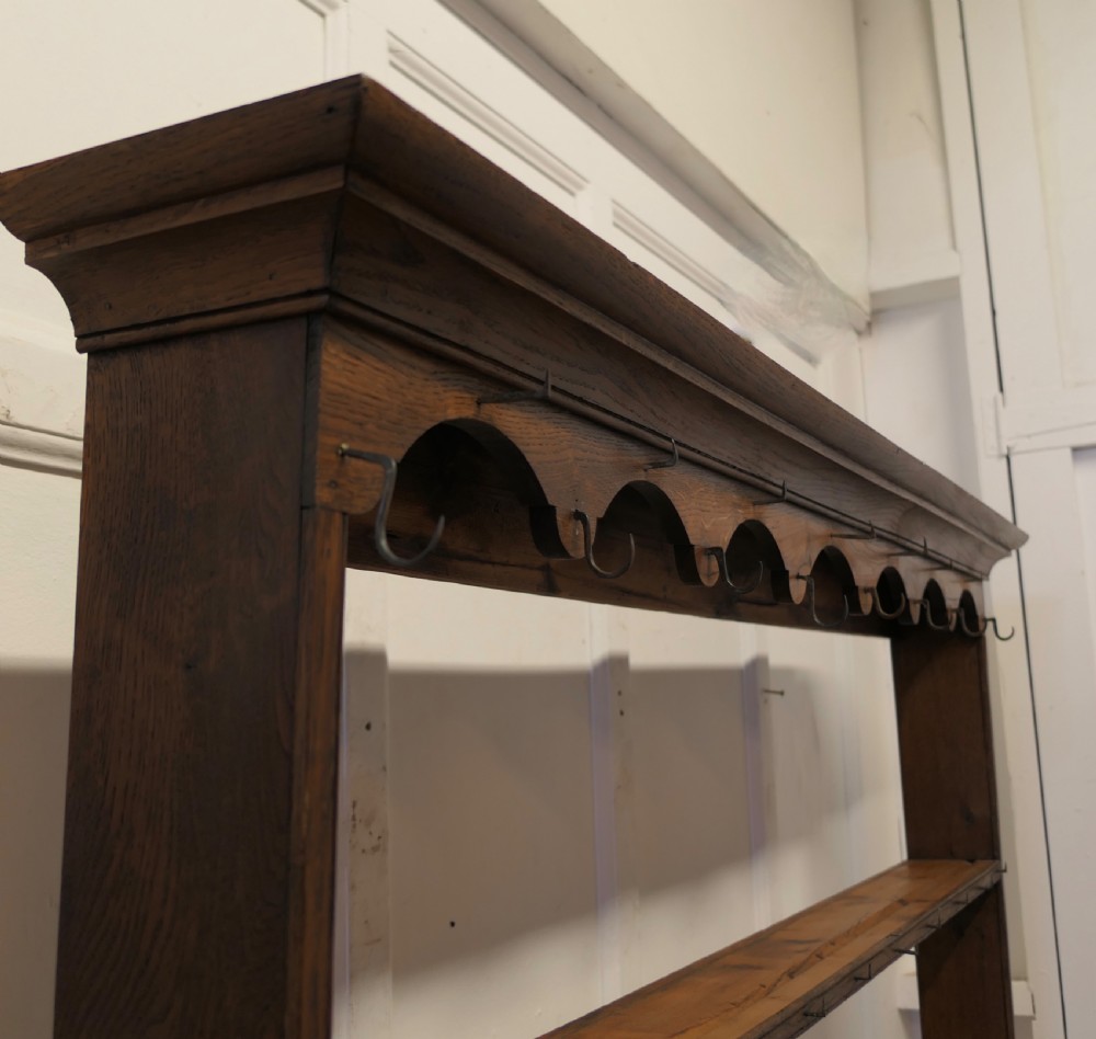 A Georgian country oak dresser featuring an open tiered plate rack set above multiple drawer compartments, arched aprons, and an open pot shelf at the base. View VI
