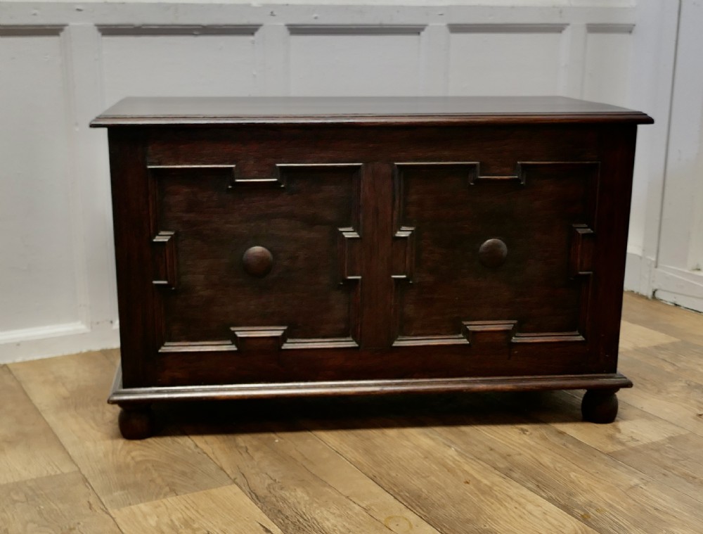 A dark oak panelled coffer featuring geometric moulded panels with central raised circular bosses, resting on bun feet.
