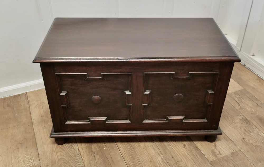 A dark oak panelled coffer featuring geometric moulded panels with central raised circular bosses, resting on bun feet. View II
