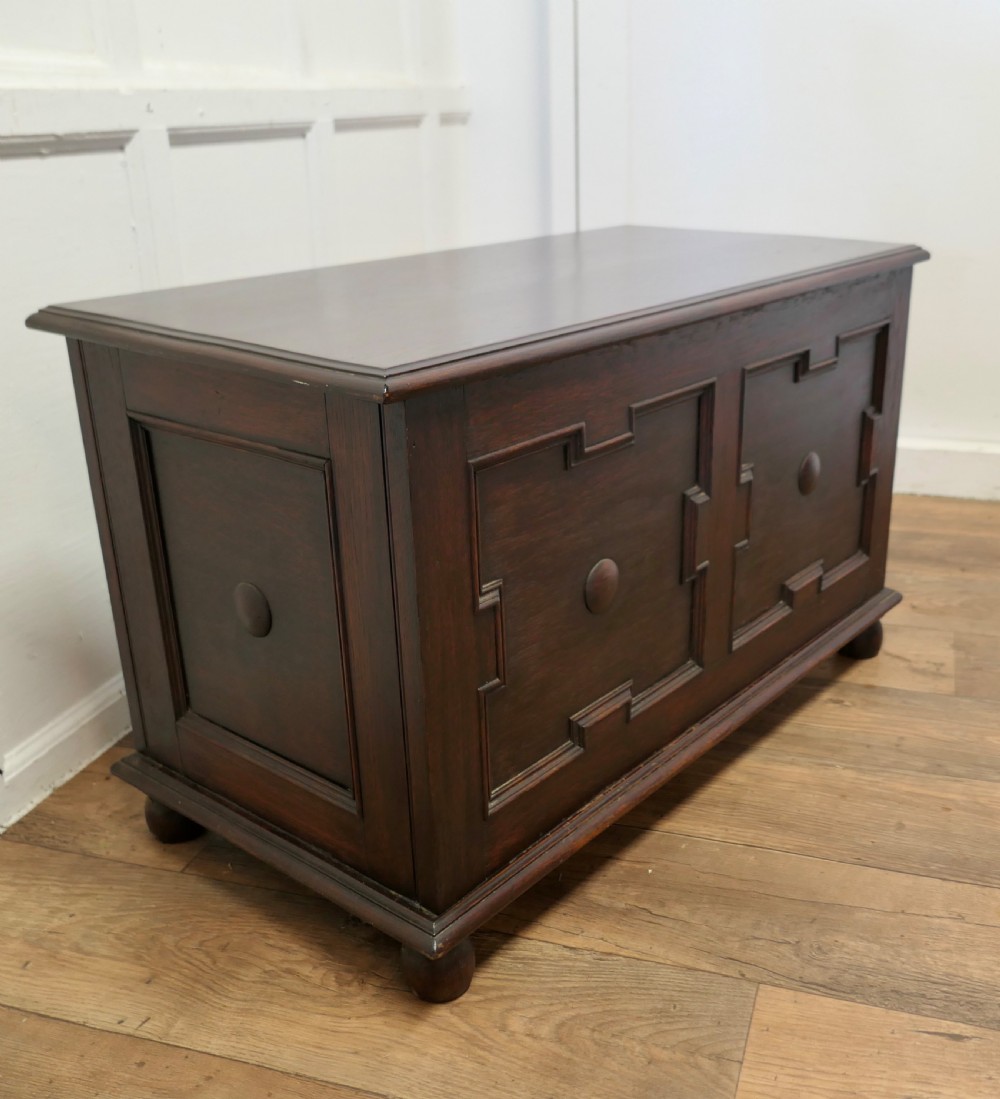 A dark oak panelled coffer featuring geometric moulded panels with central raised circular bosses, resting on bun feet. View III