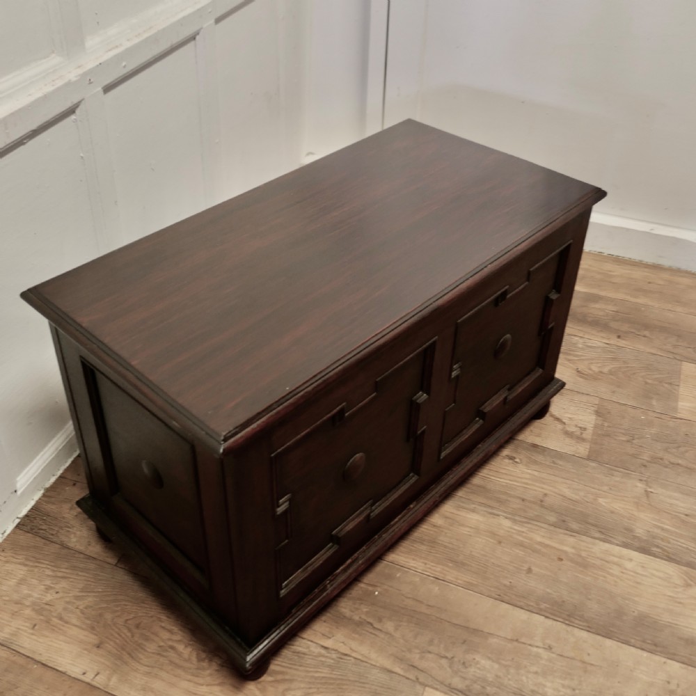 A dark oak panelled coffer featuring geometric moulded panels with central raised circular bosses, resting on bun feet. View V