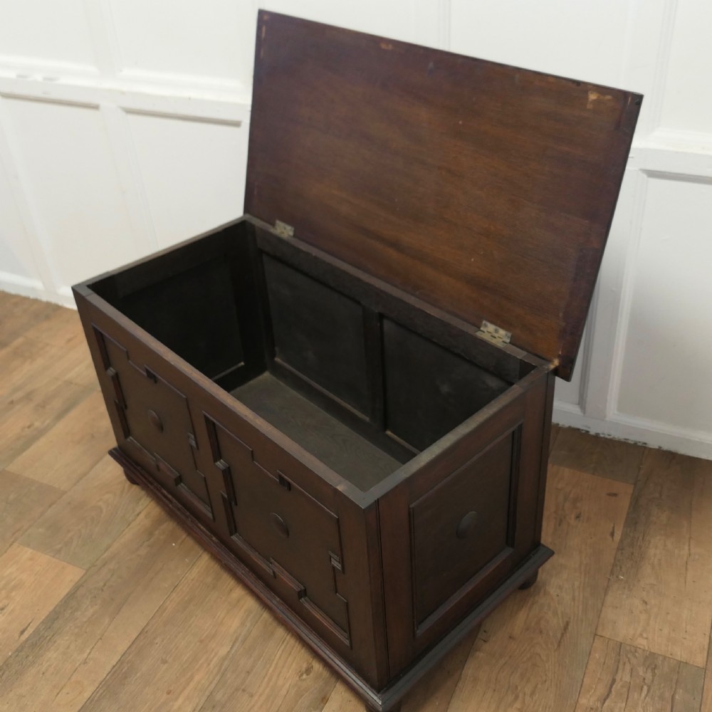 A dark oak panelled coffer featuring geometric moulded panels with central raised circular bosses, resting on bun feet. View VI