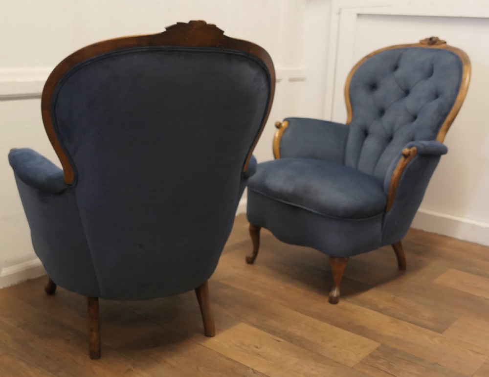 A pair of French salon armchairs upholstered in blue button-backed velvet with carved walnut frames and short wooden legs.