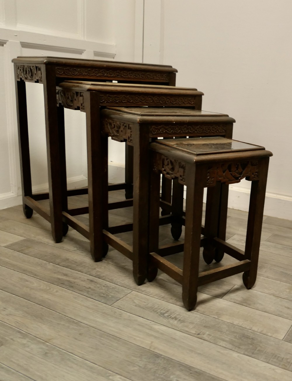 A set of four dark brown hardwood nesting tables featuring carved pierced aprons and glass-inset tops.