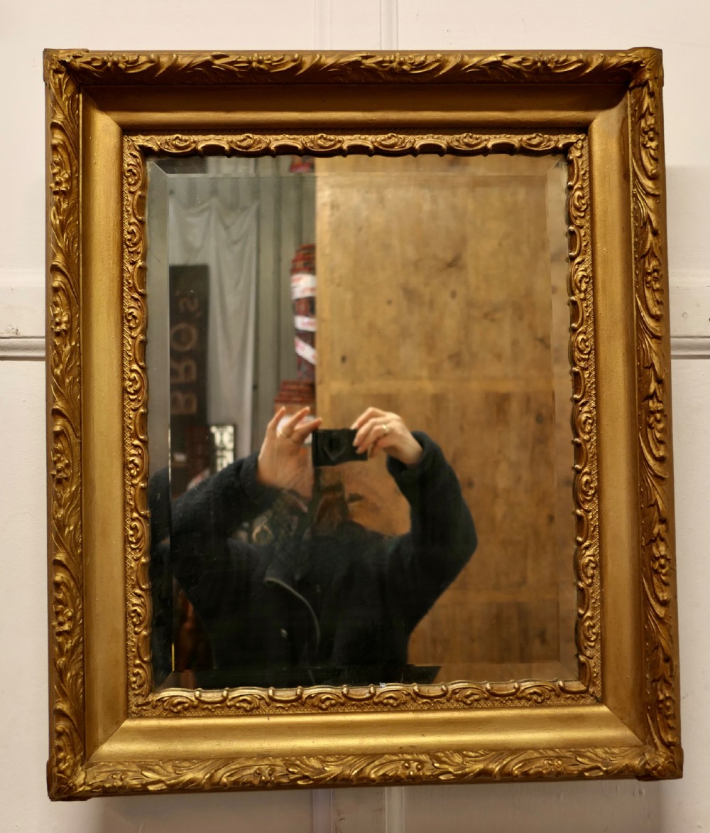 A rectangular antique giltwood wall mirror featuring ornate relief foliage moulding and a bevelled glass plate. View III