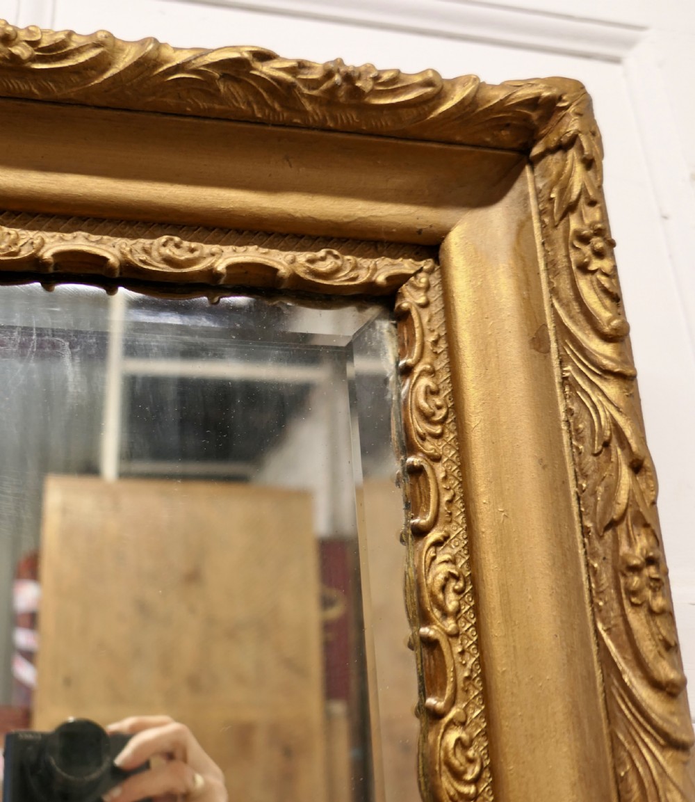 A rectangular antique giltwood wall mirror featuring ornate relief foliage moulding and a bevelled glass plate. View V