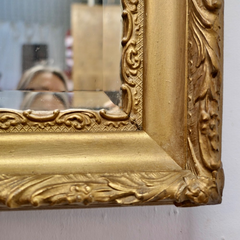 A rectangular antique giltwood wall mirror featuring ornate relief foliage moulding and a bevelled glass plate. View VII