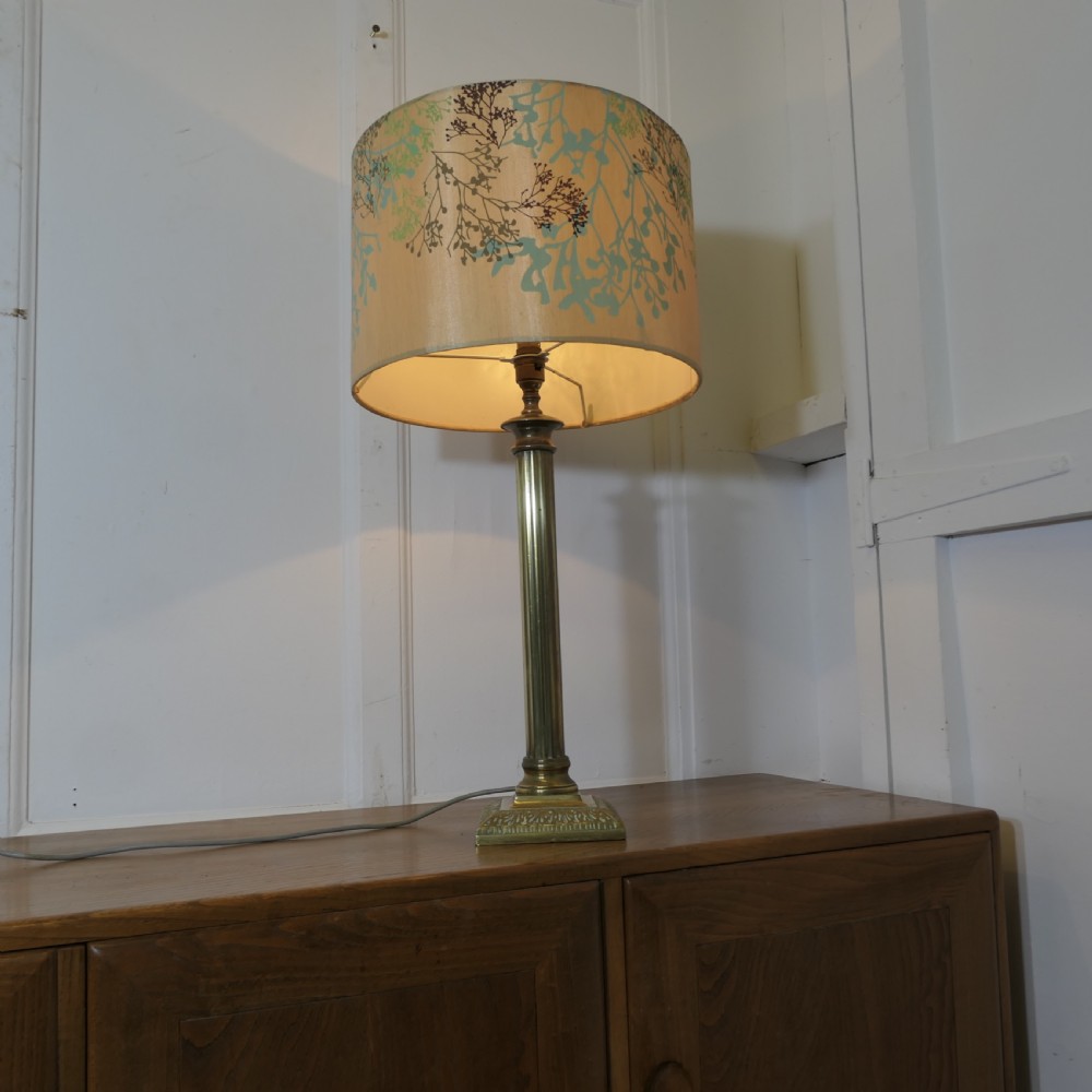A tall brass table lamp featuring a fluted column stem on a stepped square base, topped with a cylindrical cream shade patterned with botanical motifs. View II