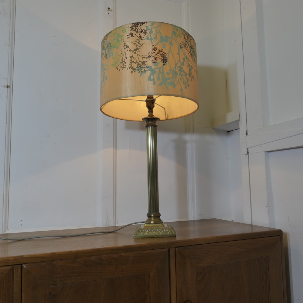 A tall brass table lamp featuring a fluted column stem on a stepped square base, topped with a cylindrical cream shade patterned with botanical motifs. View III