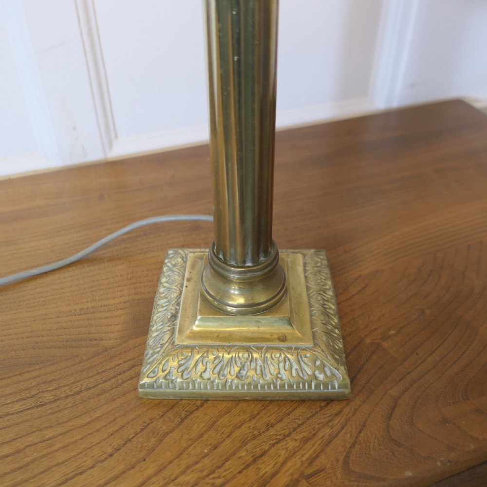 A tall brass table lamp featuring a fluted column stem on a stepped square base, topped with a cylindrical cream shade patterned with botanical motifs. View V