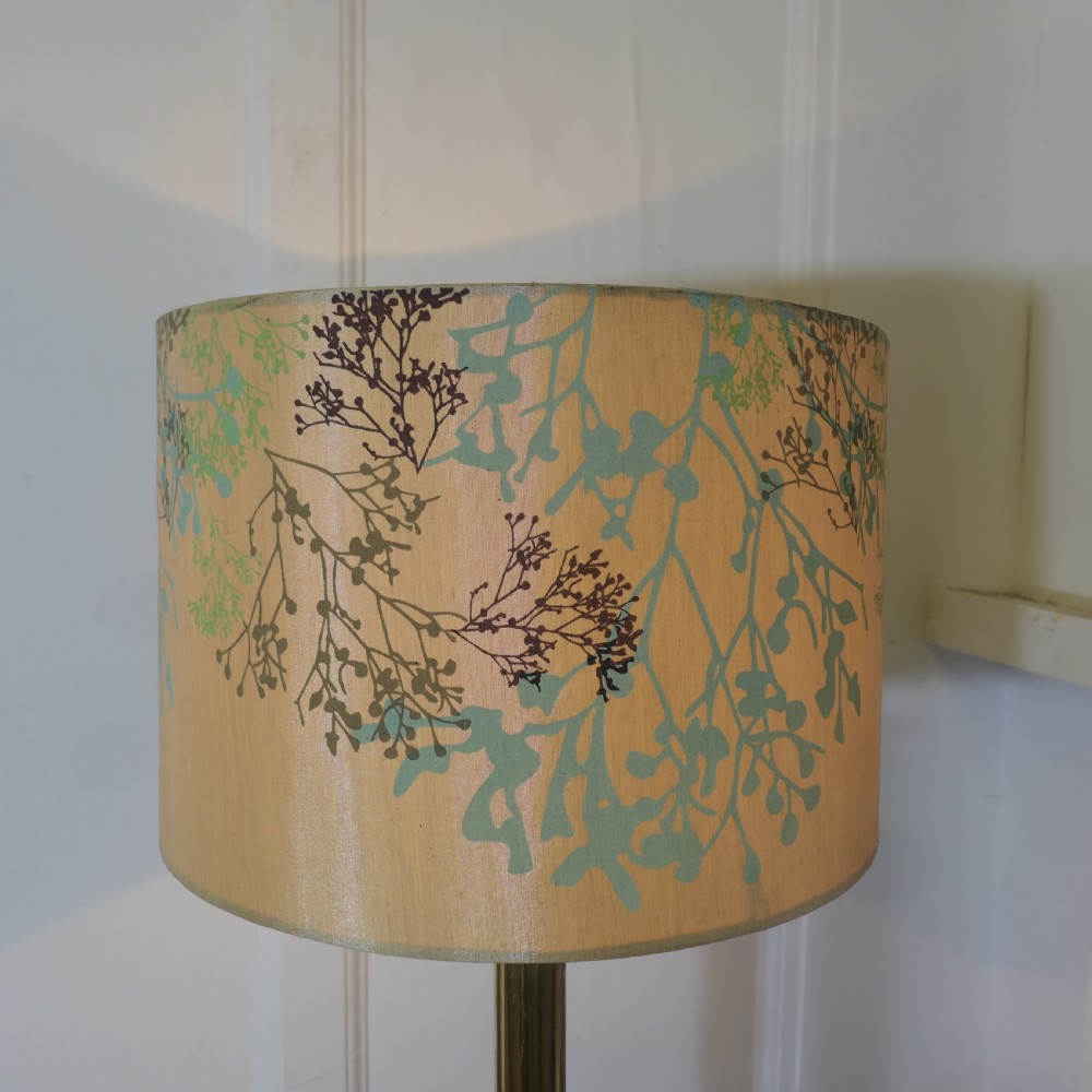 A tall brass table lamp featuring a fluted column stem on a stepped square base, topped with a cylindrical cream shade patterned with botanical motifs. View VI